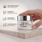 CBD Skin Repair Cream jar with hand holding it on a light background