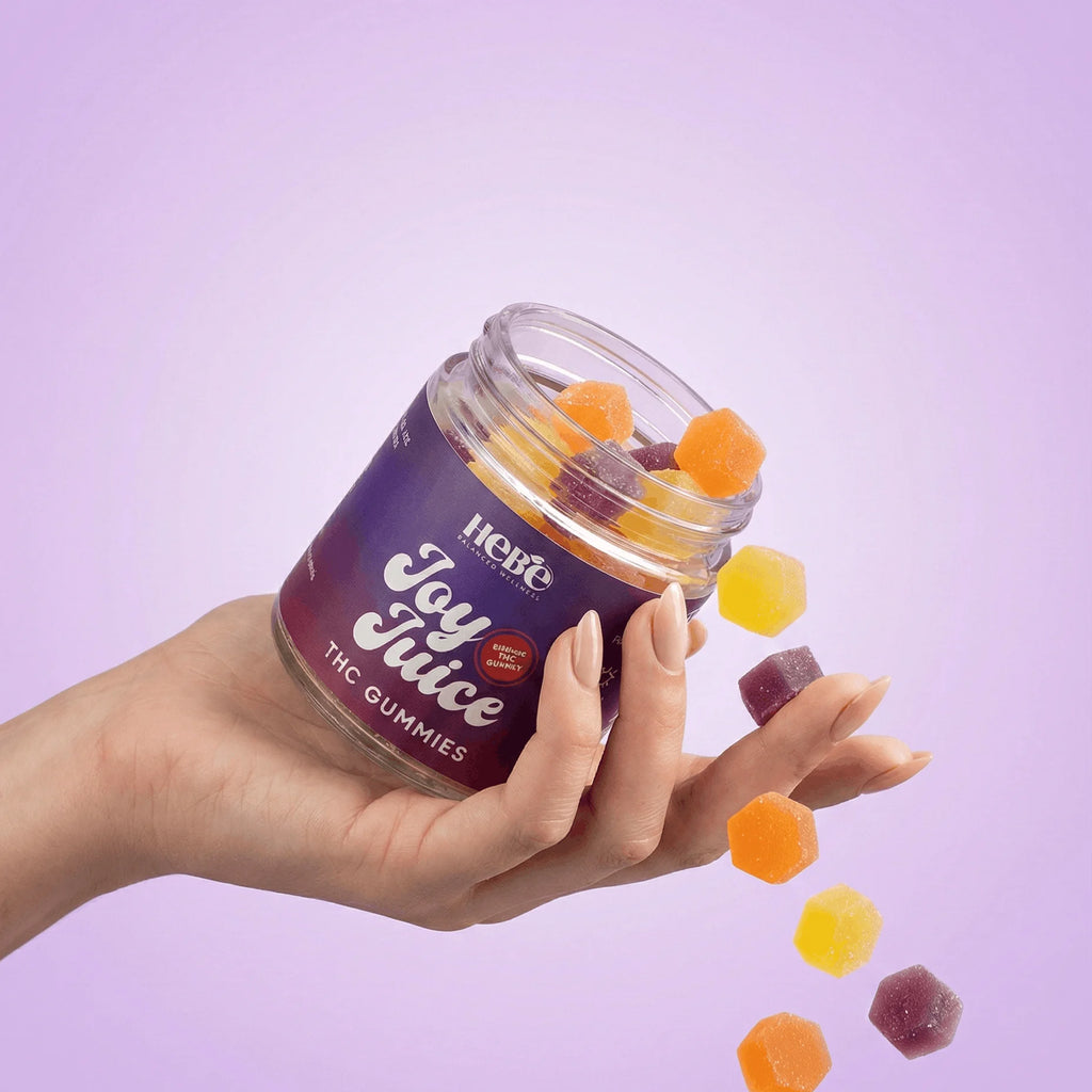Hand holding a jar of 'Hebe Joy Juice THC Gummies' with gummies spilling out on a purple background